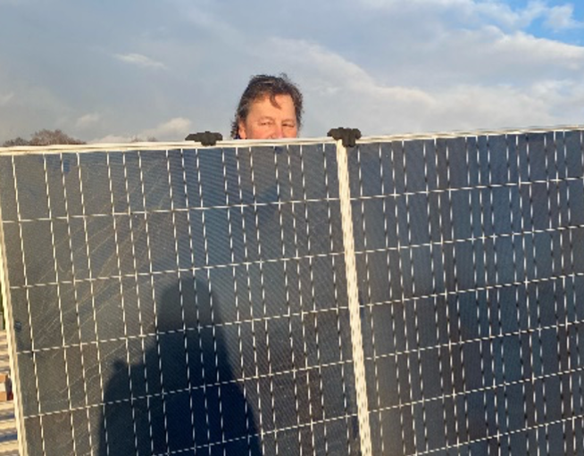 Ein Mann, dessen halbes Gesicht hinter den Solarmodulen hervor schaut.